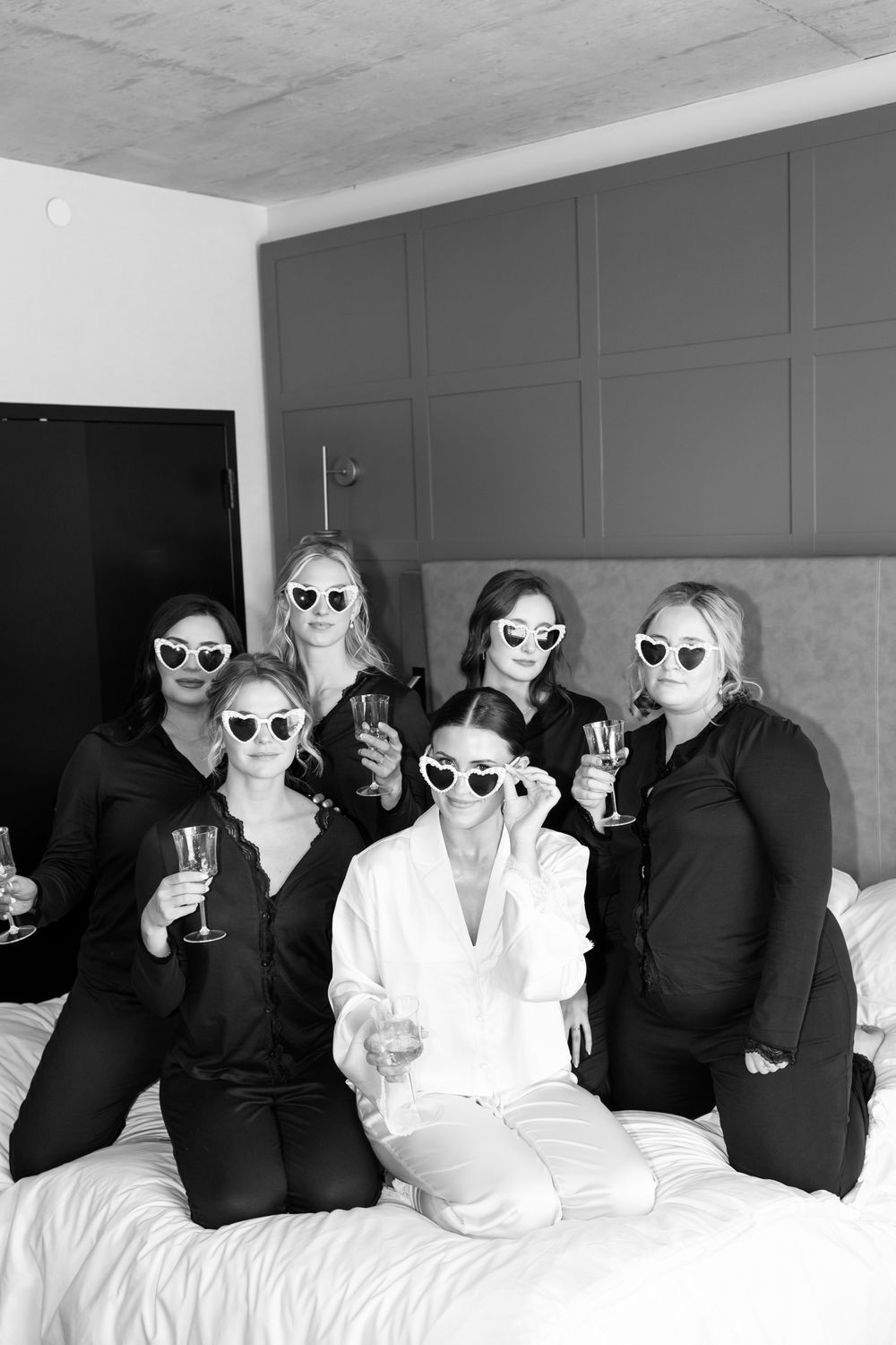 Wedding party wearing sunglasses poses together on white couch.