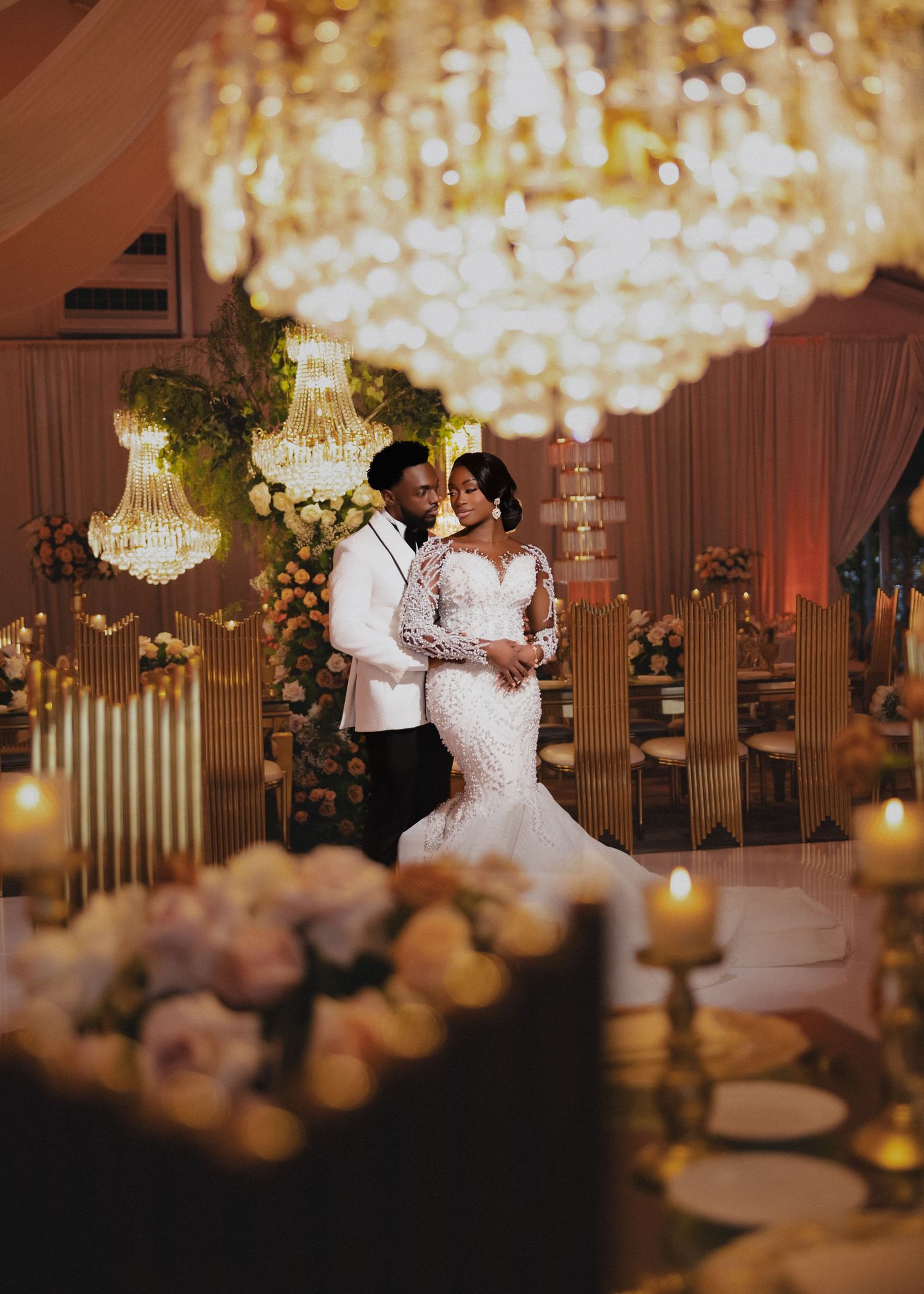 Elegant wedding reception venue with crystal chandeliers and couples dancing on the dance floor in warm lighting.