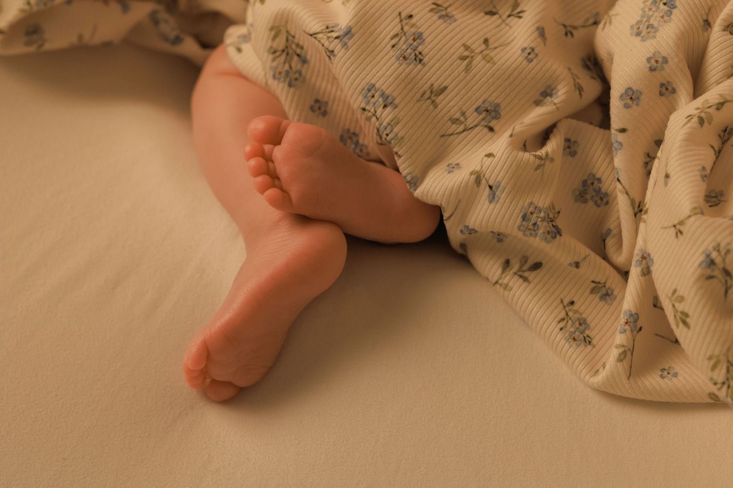 Close-up view of tiny baby feet against a soft floral patterned fabric background.