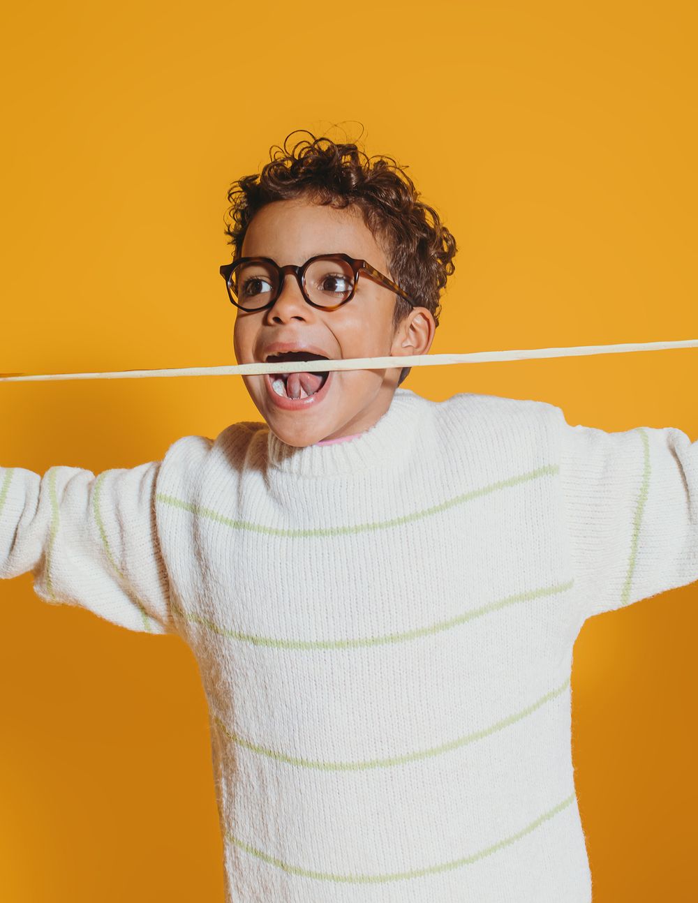 Playful figure in white sweater poses with arms outstretched against vibrant orange background.