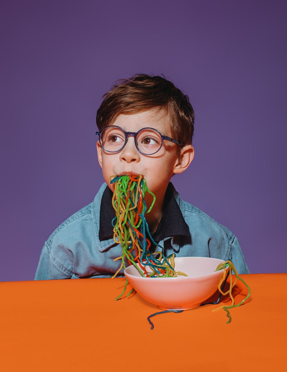 A playful sequence of someone eating colorful pasta noodles against a purple and orange background.