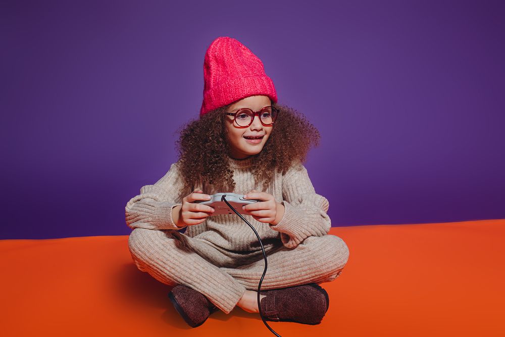 A person wearing glasses and a red beanie plays with a mobile device against a purple and orange background.