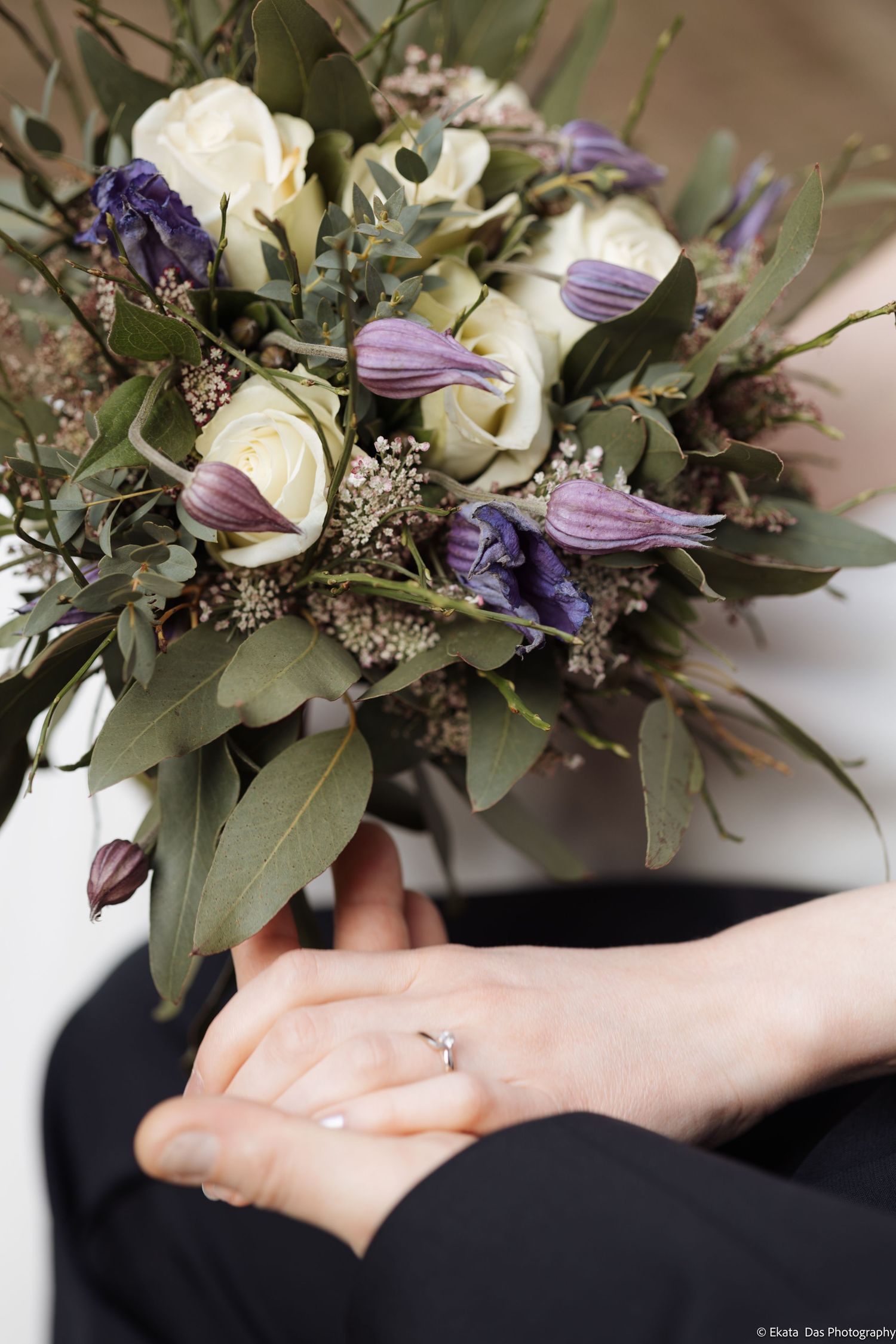 Delicate wedding bouquet featuring purple flowers and greenery with engagement ring detail.