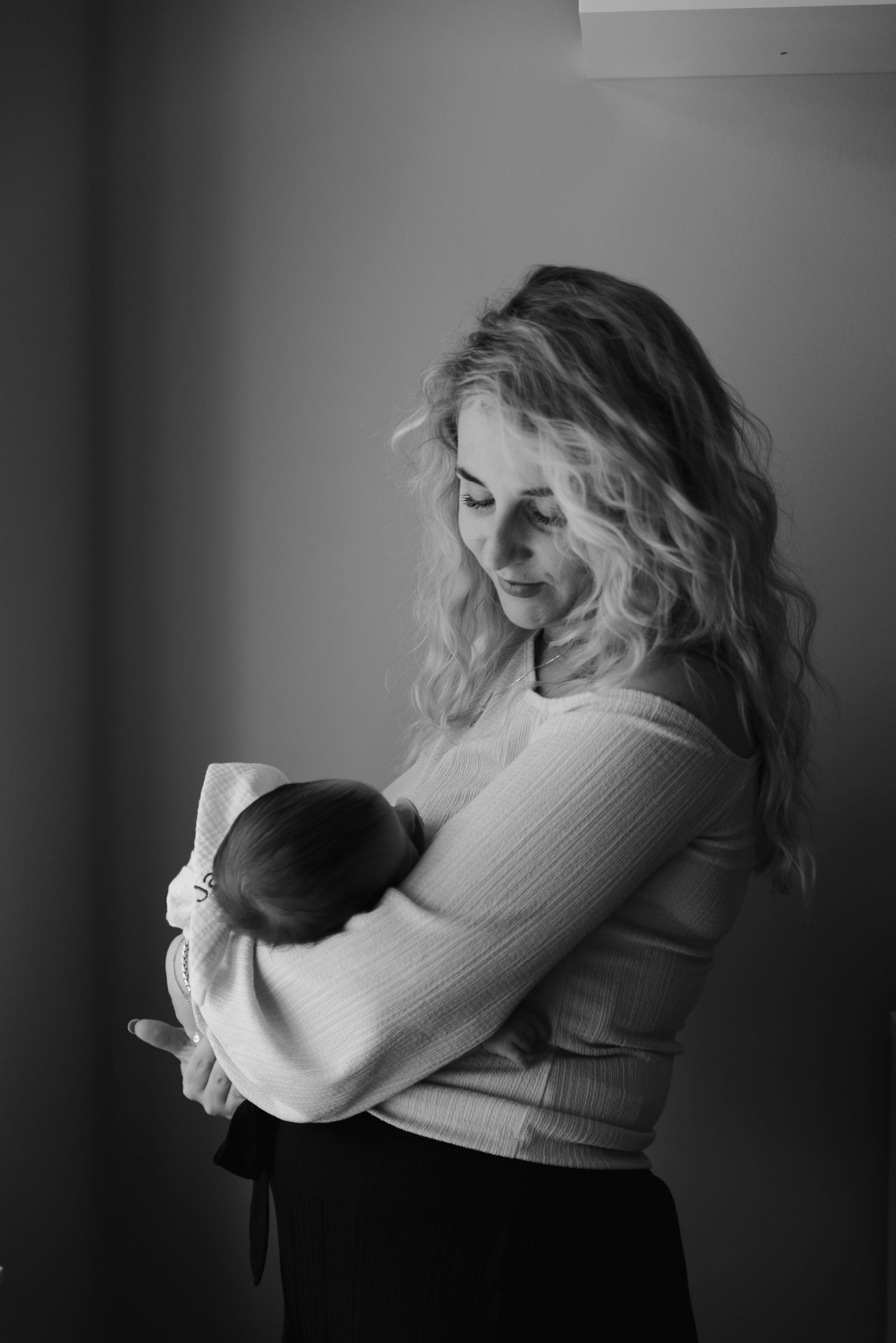 Intimate black and white portrait showing nurturing moment with newborn in soft window light.