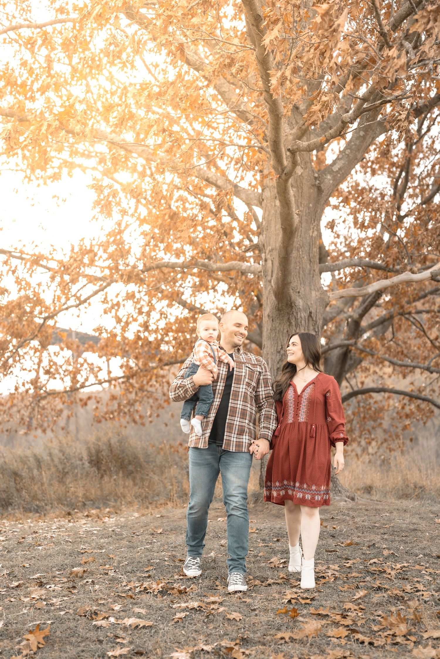 A couple walks hand in hand through autumn trees with golden leaves during a fall photo session.