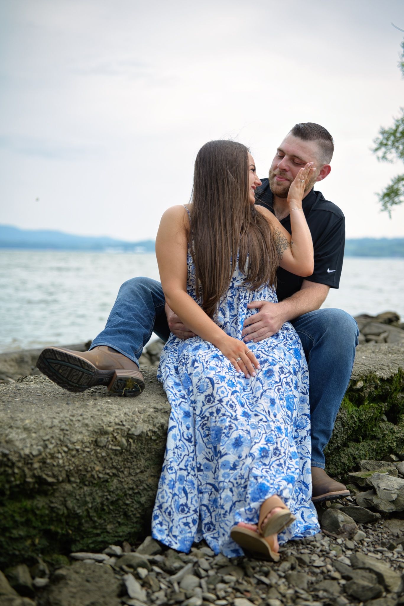 A couple shares an intimate moment together on rocky beach shoreline wearing blue and black clothing.