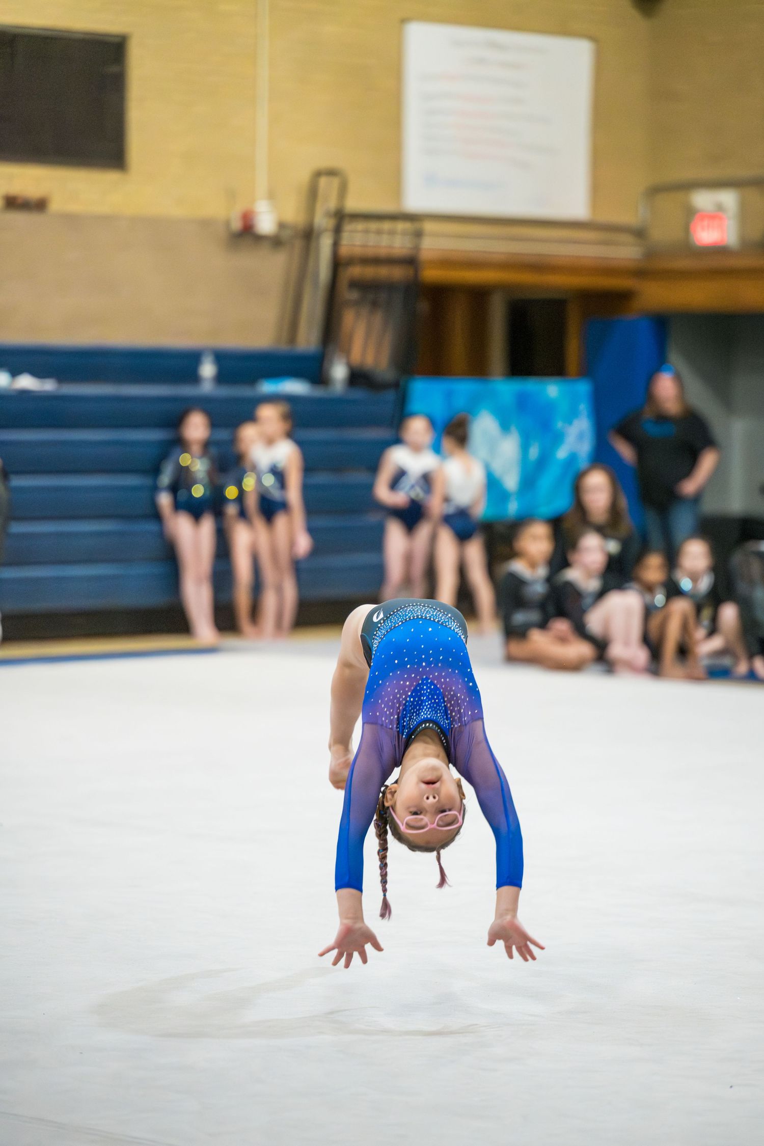 A sequence of four photos showing a gymnast performing a front walkover on a white mat in a gymnasium.