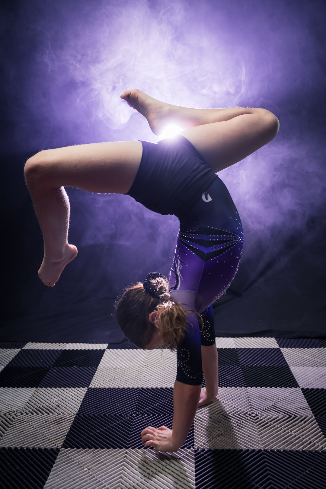 Gymnast performs a fluid handstand sequence in a dark studio with dramatic purple lighting and checkered floor mats.
