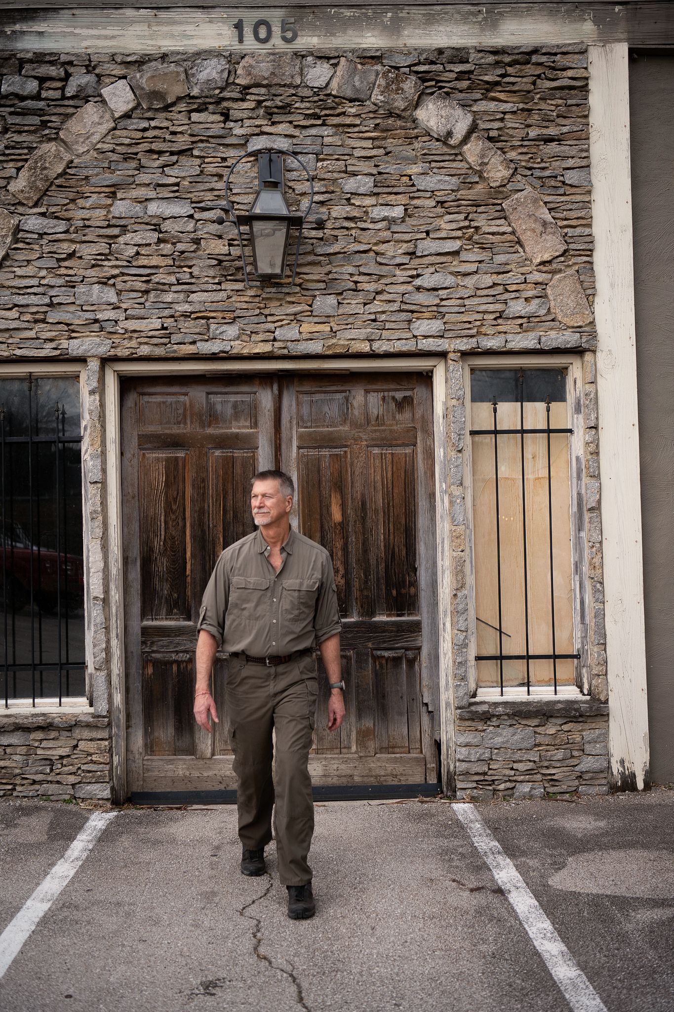 A sequence of four photos showing a person in olive workwear walking past a rustic stone building with wooden doors.