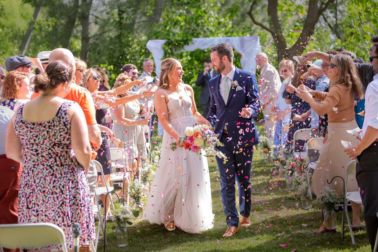 Couple celebrating while walking up the aisle after saying I Do with loved ones throwing flowers petals