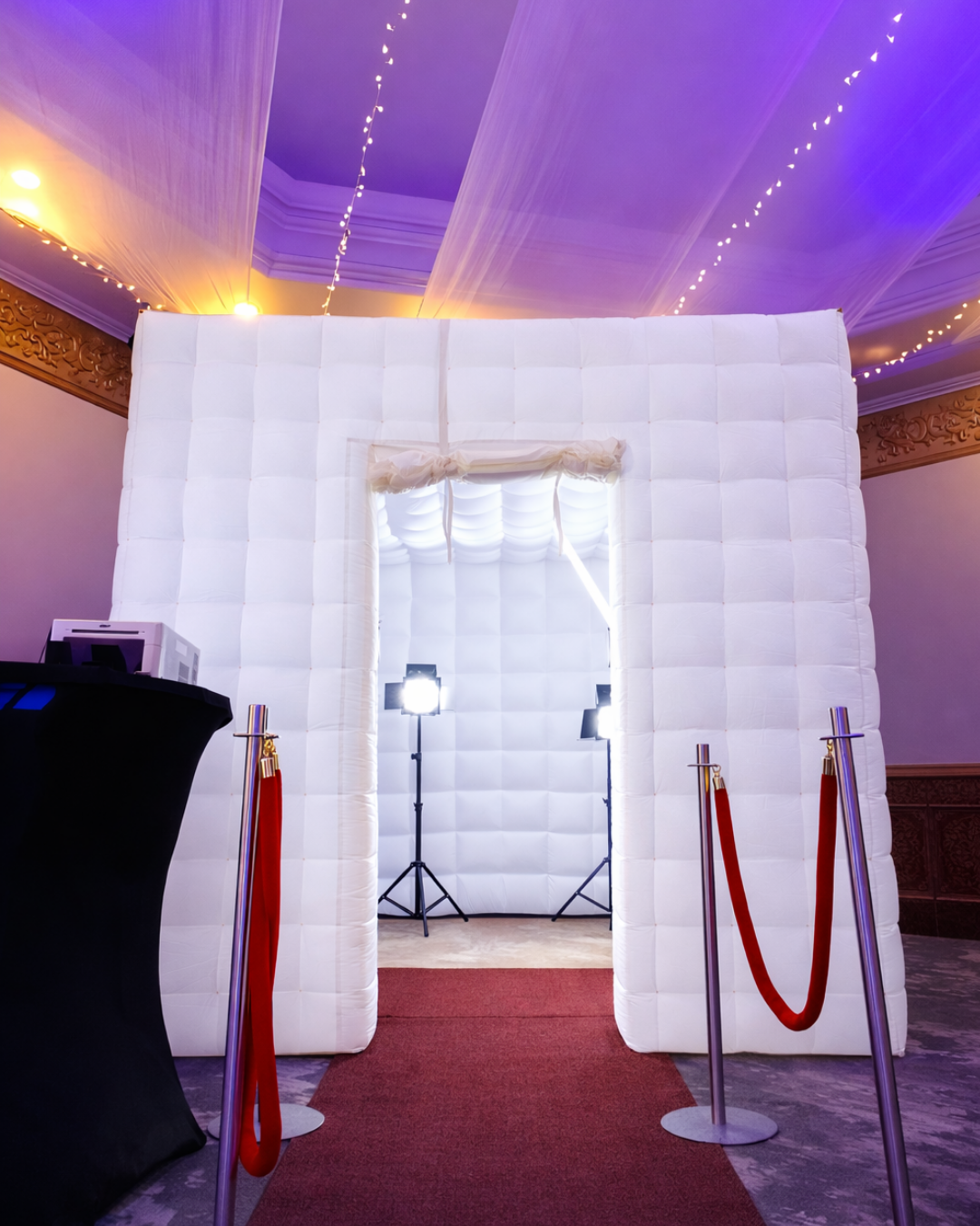 An illuminated white inflatable maze structure with red fabric accents and string lights creates an ethereal event space.