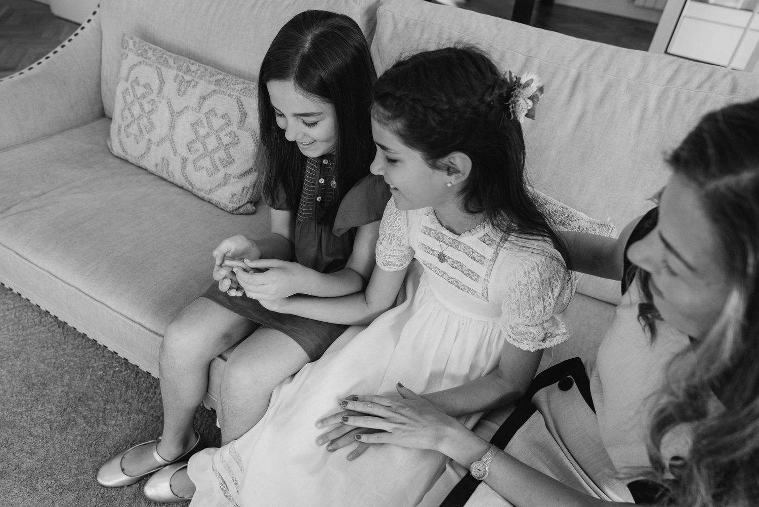 A black and white photo shows a person in white dress sitting on a bed in a minimalist room.