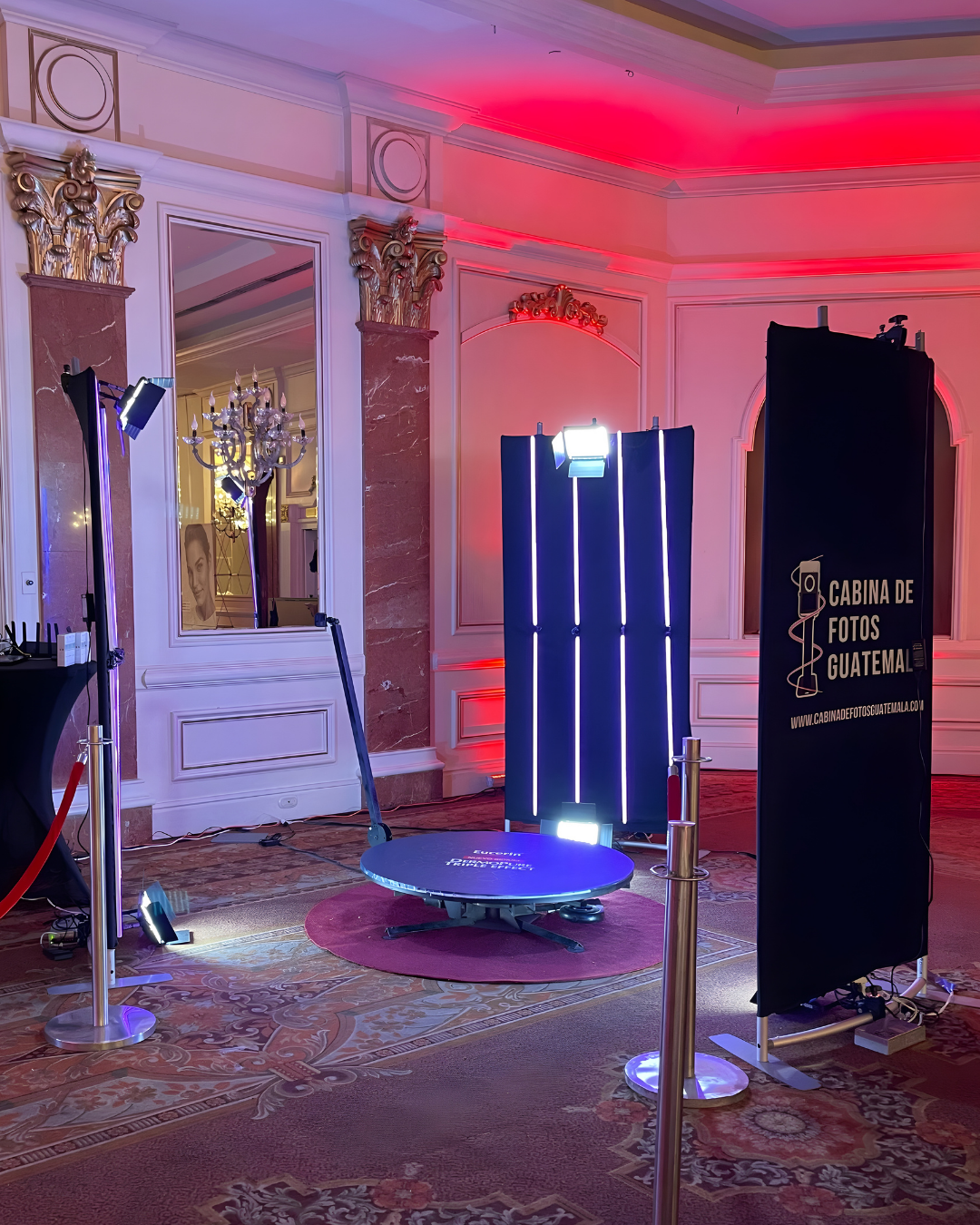 Photo booth setup with black curtains and red ambient lighting in an elegant ballroom with ornate decor and patterned carpet.