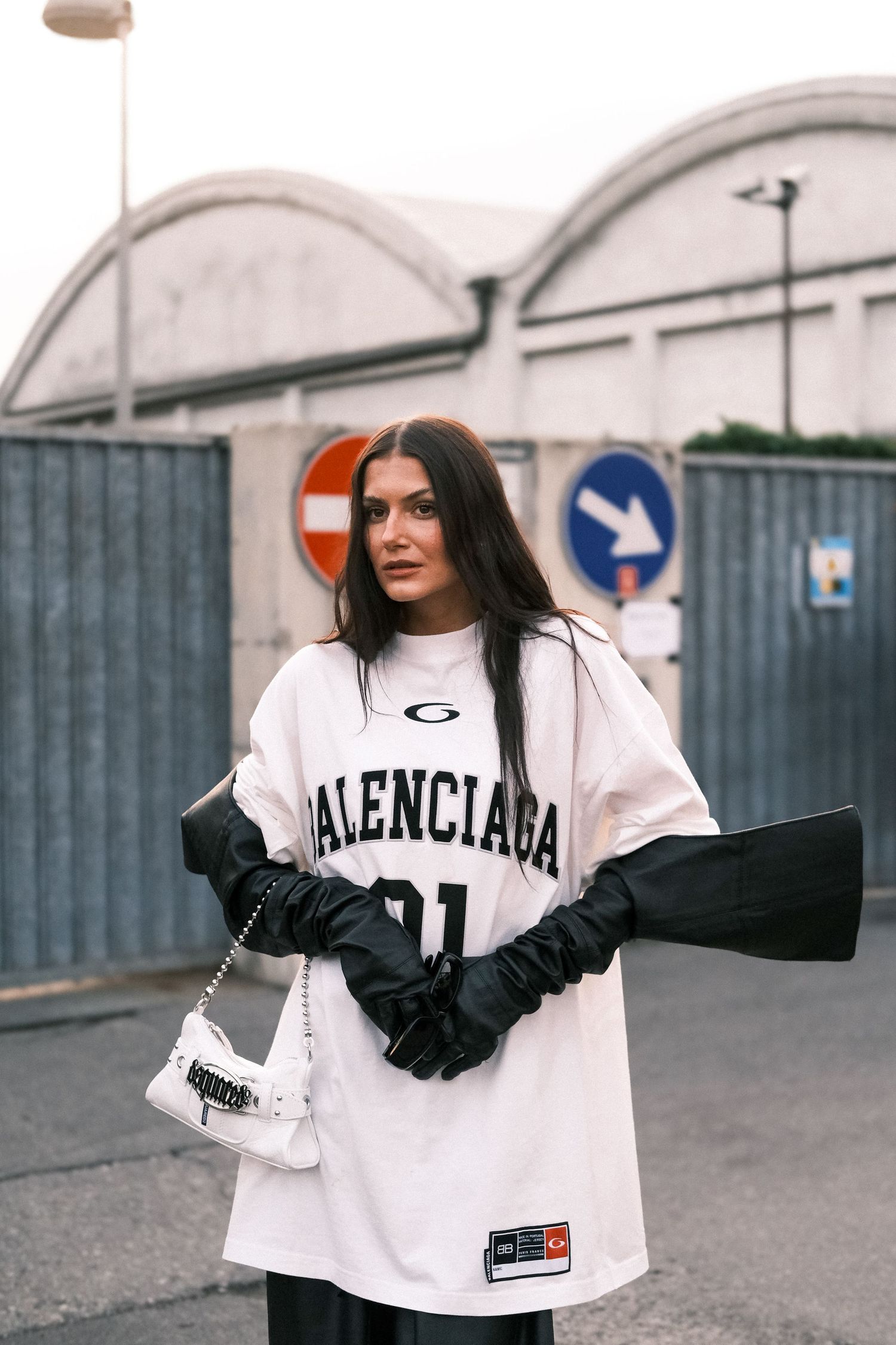 Street style fashion featuring white Balenciaga sweatshirt with black gloves and urban backdrop.