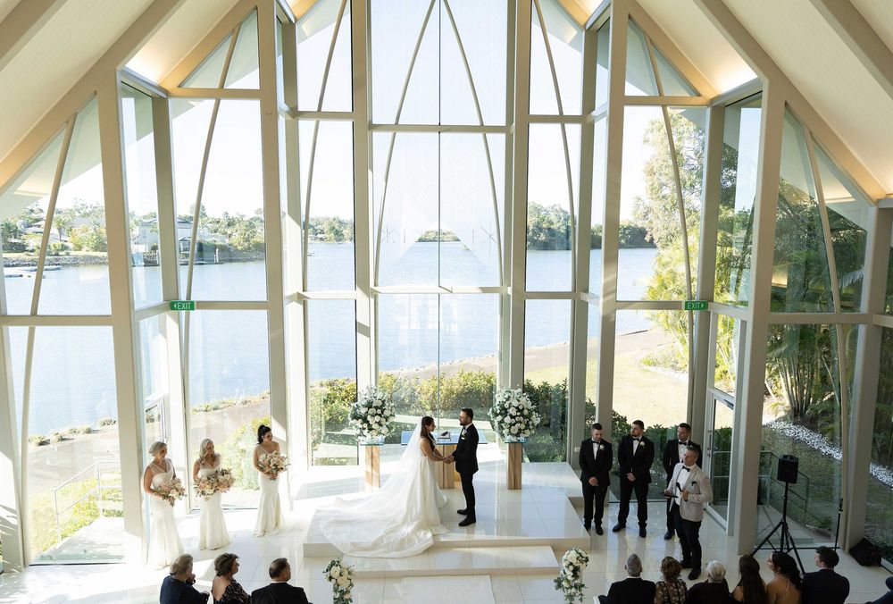 Elegant wedding ceremony inside a stunning glass chapel overlooking a serene waterfront.