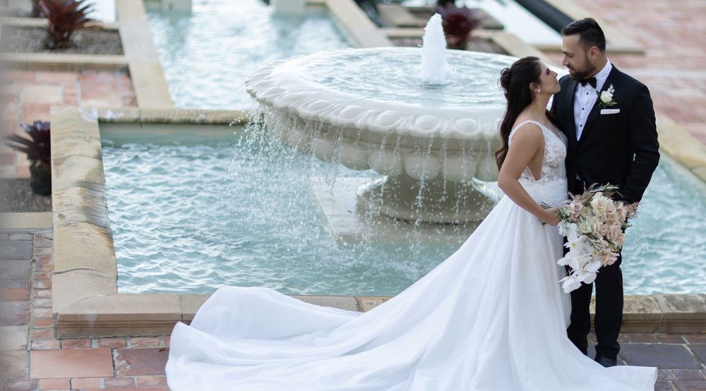 Bride and groom share a romantic moment beside an ornate fountain at their wedding venue.