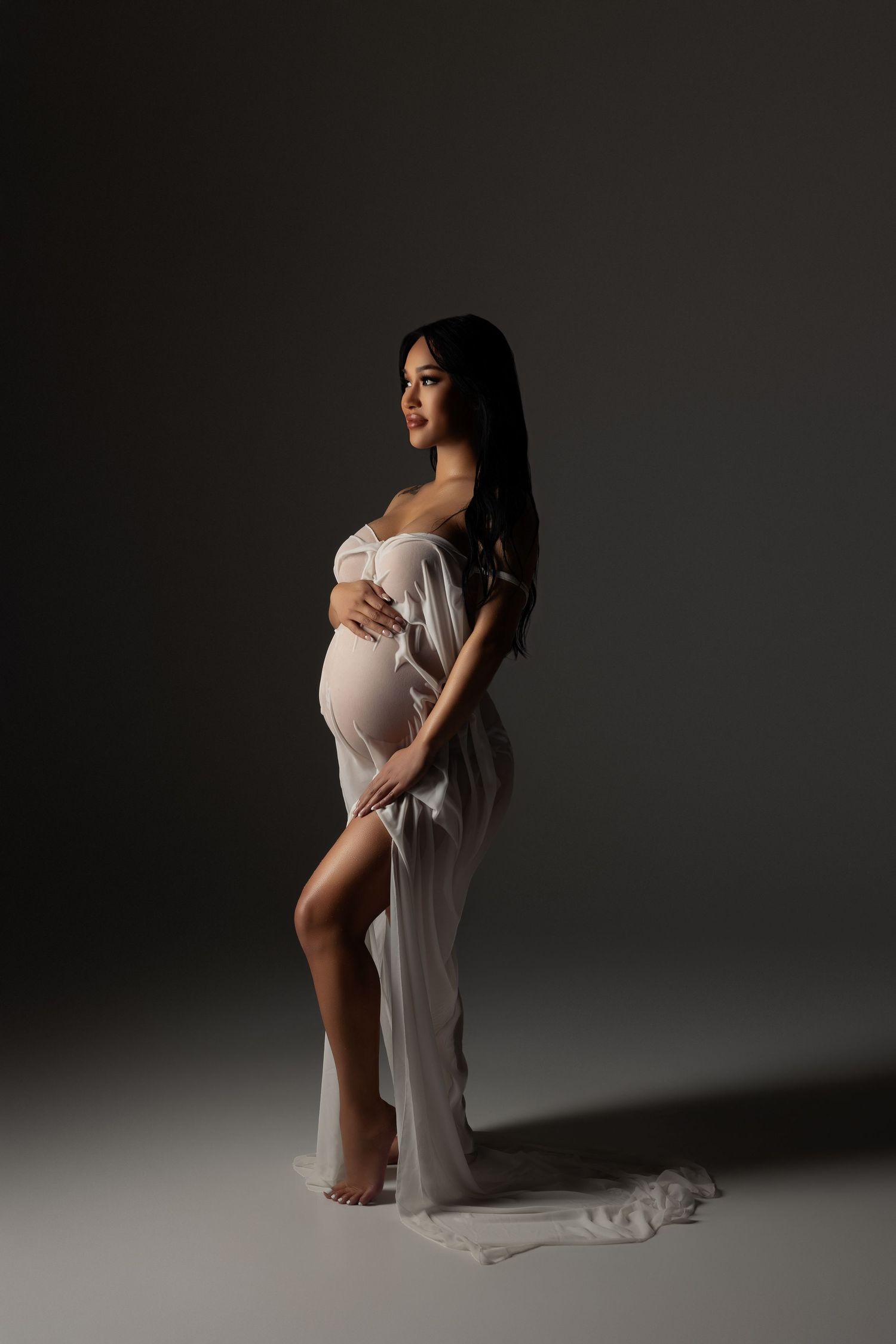 Artistic maternity photo series showing silhouetted figures in white fabric against dark background in dramatic poses.