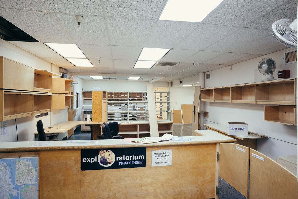 Interior view of an empty commercial space with fluorescent lighting and wooden cabinets along the walls.