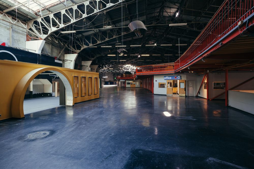 Industrial warehouse ceiling with exposed metal beams, ductwork, and lighting fixtures.