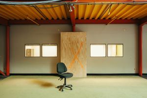 Industrial office space with orange ceiling beams, white walls, and a lone office chair.
