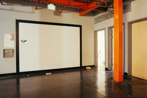 Empty office space with white walls, dark flooring, and an orange support column.