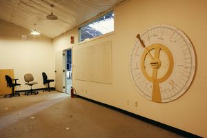 Office space with large circular clock design painted on beige wall.