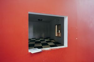 Checkerboard floor visible through red-framed window opening.