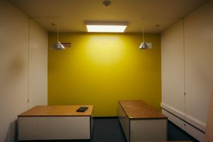 Small office room with bright yellow accent wall and wooden desks.