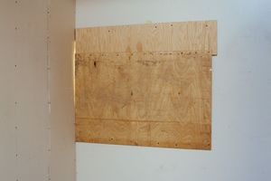 Row of plywood panels mounted on white walls in an empty room.
