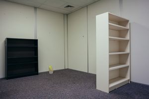 Empty office space with white walls, drop ceiling, and built-in shelving units.