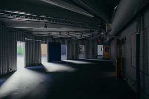 Dark industrial corridor with exposed ceiling and dramatic lighting creating shadows and depth.