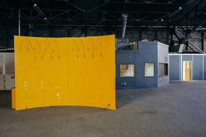 Large yellow curved wall panel in an industrial space with grey doors and concrete floor.