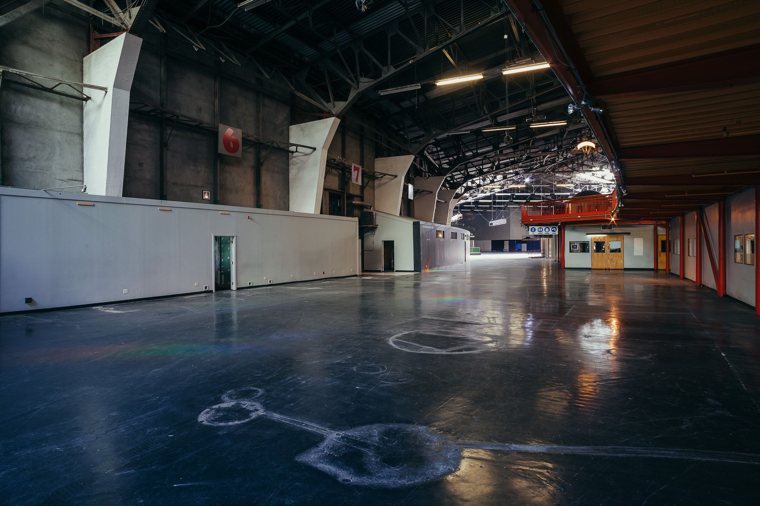 Dark empty indoor space with exposed industrial ceiling and reflective floor surface.