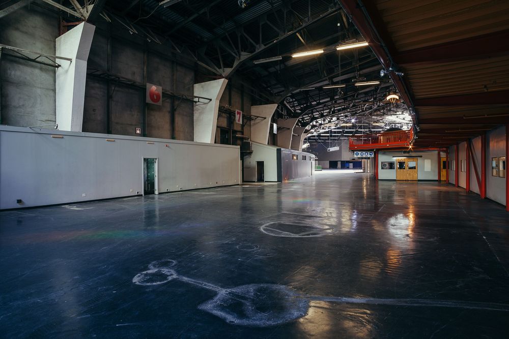 Dark empty indoor space with exposed industrial ceiling and reflective floor surface.