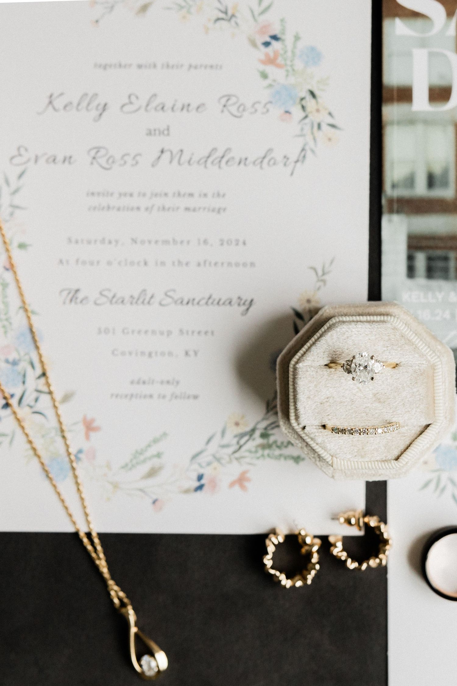 Wedding invitation with delicate floral details displayed alongside jewelry pieces and a velvet ring box.
