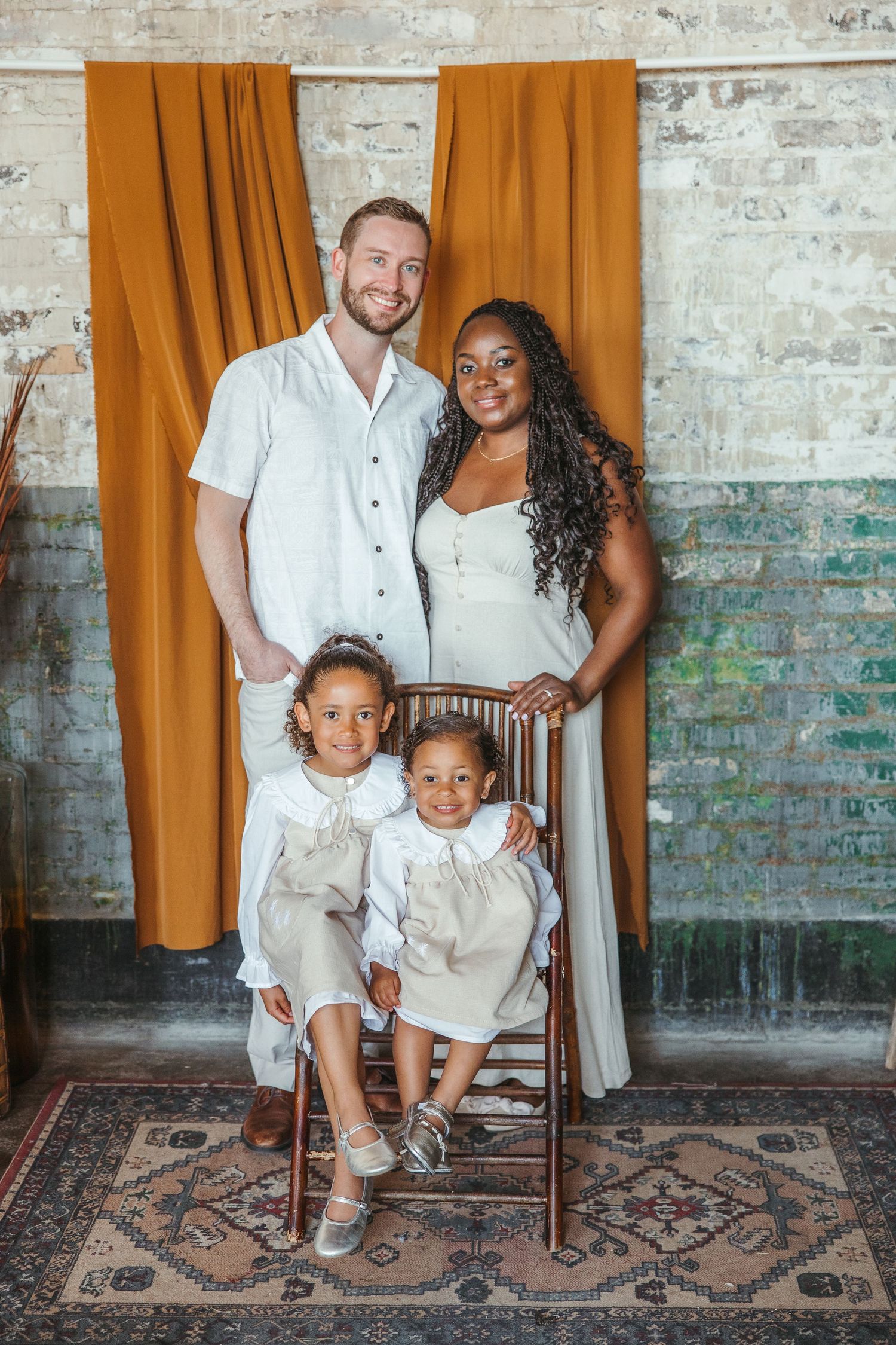 Happy interracial family of four posing before orange curtain and rustic brick wall backdrop.