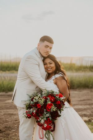 A couple in wedding attire sharing an intimate moment with a vibrant red bouquet.