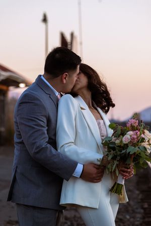 A romantic wedding kiss at sunset with the bride holding a beautiful floral bouquet.