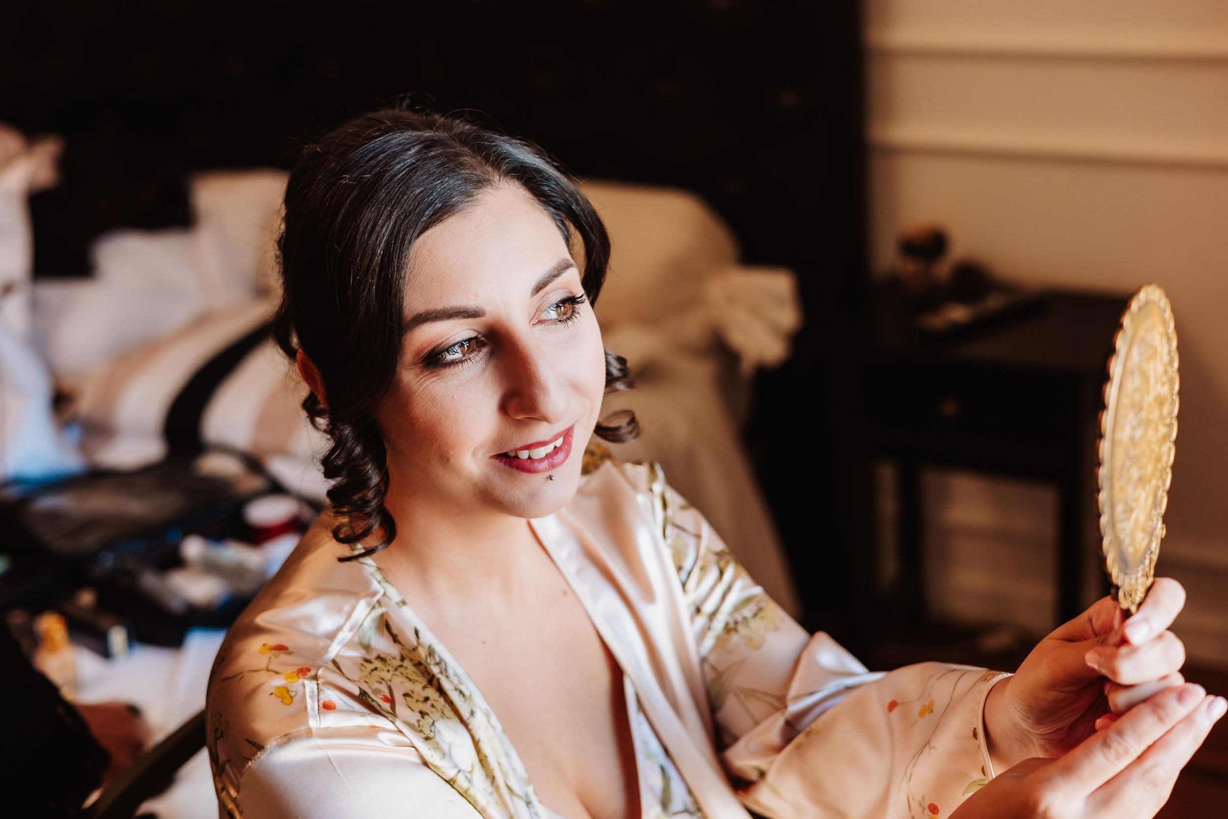 A person in a silk robe holds up a handheld mirror while getting ready in a dressing room.
