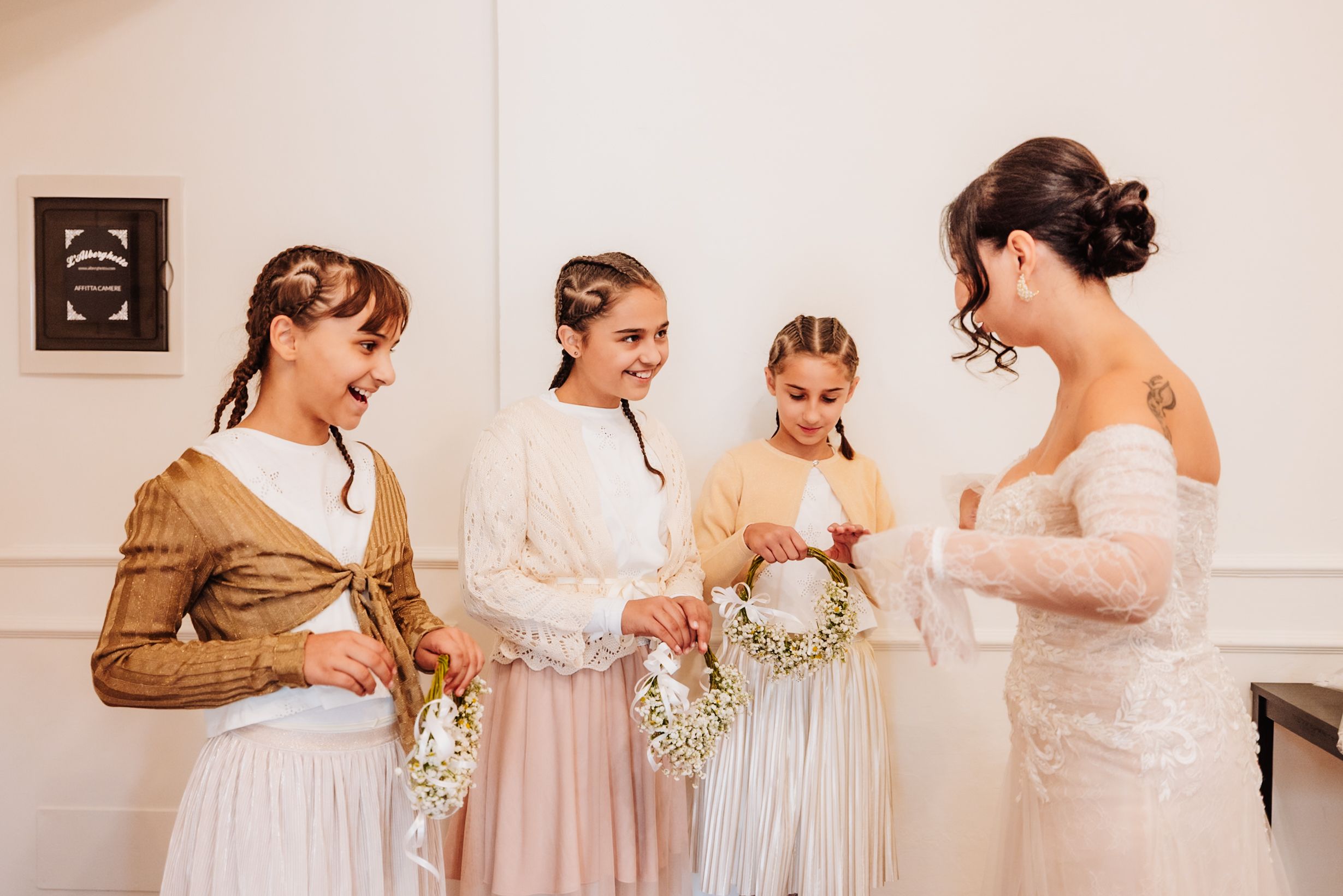 Bridesmaids in pastel dresses gather together holding small white bouquets before a wedding ceremony.