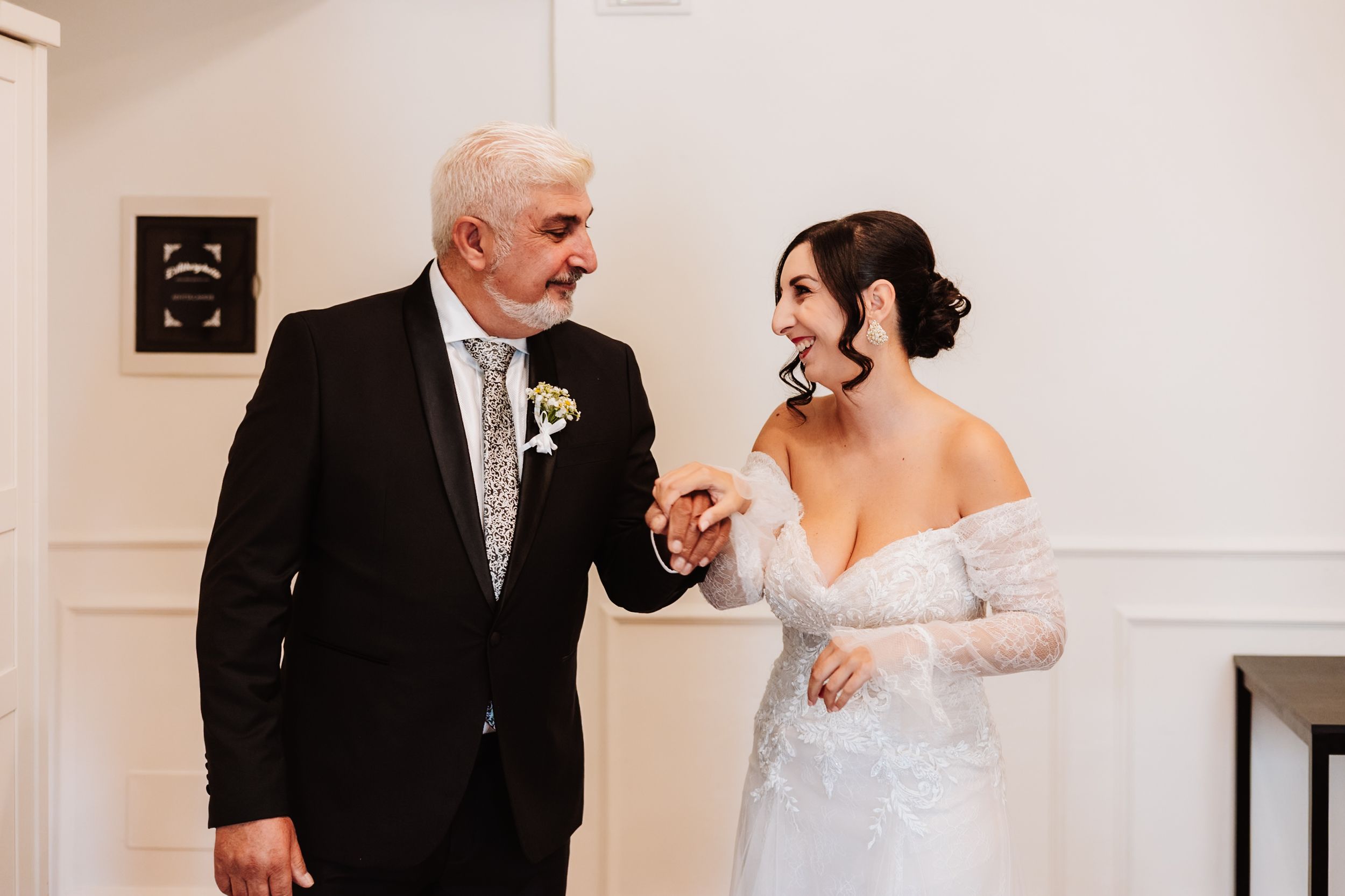 A bride and father share emotional moments before a wedding ceremony in a bright white room.