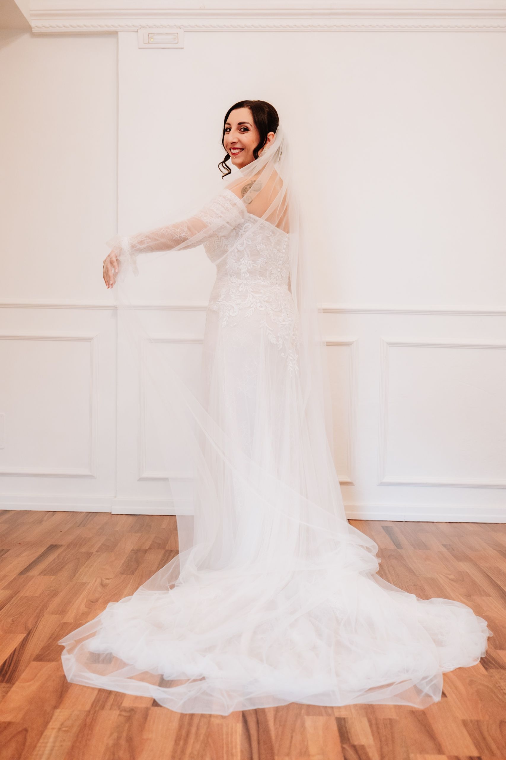 A flowing white wedding dress with a long train creates elegant movement as it sweeps across a hardwood floor.