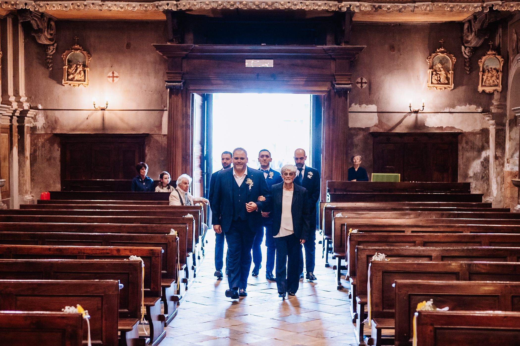 A group of people walk through a dimly lit church aisle with wooden pews and gothic architecture.