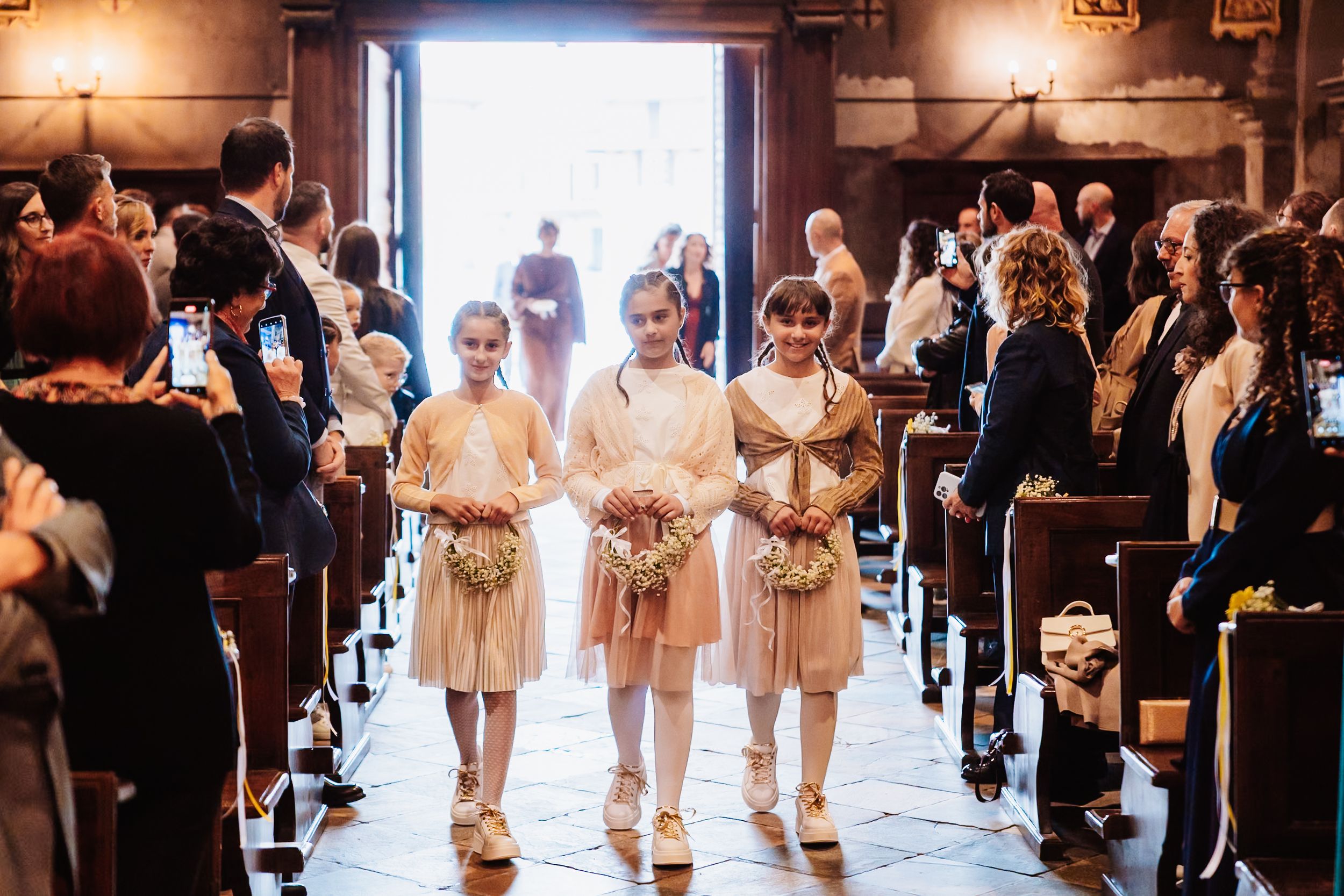 A group of bridesmaids in champagne-colored dresses walk down the aisle during a wedding ceremony.