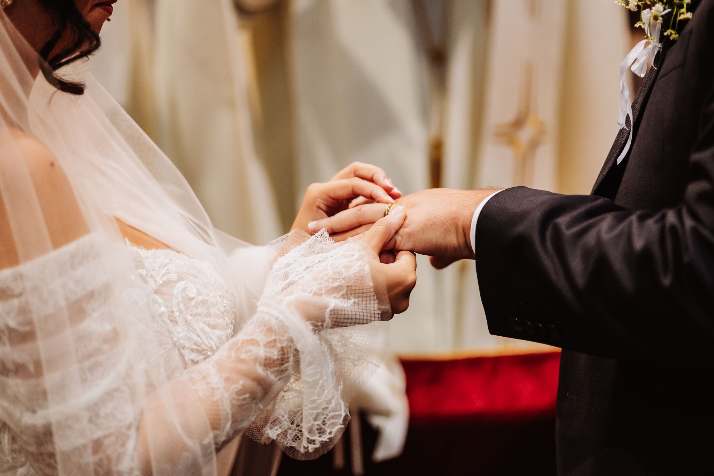 Close-up of hands exchanging wedding rings during traditional ceremony with white lace and formal attire.