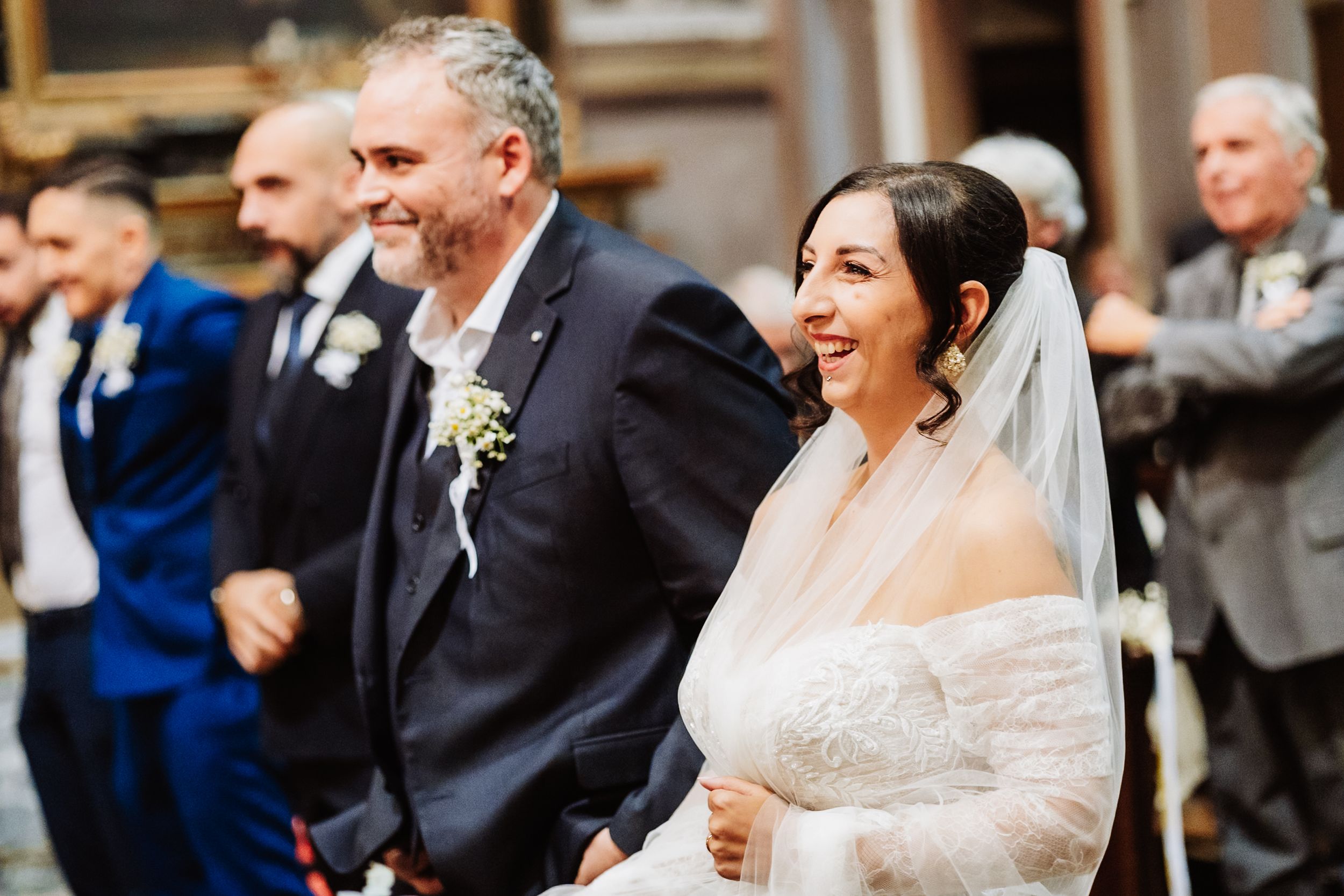 A happy couple shares a joyful moment during their wedding ceremony as guests look on in the background.