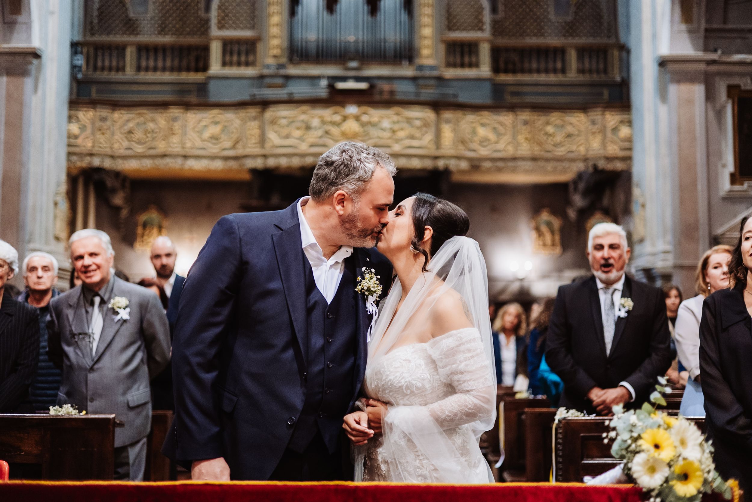 Elegant wedding ceremony takes place in a grand historic church with ornate architectural details and stained glass windows.