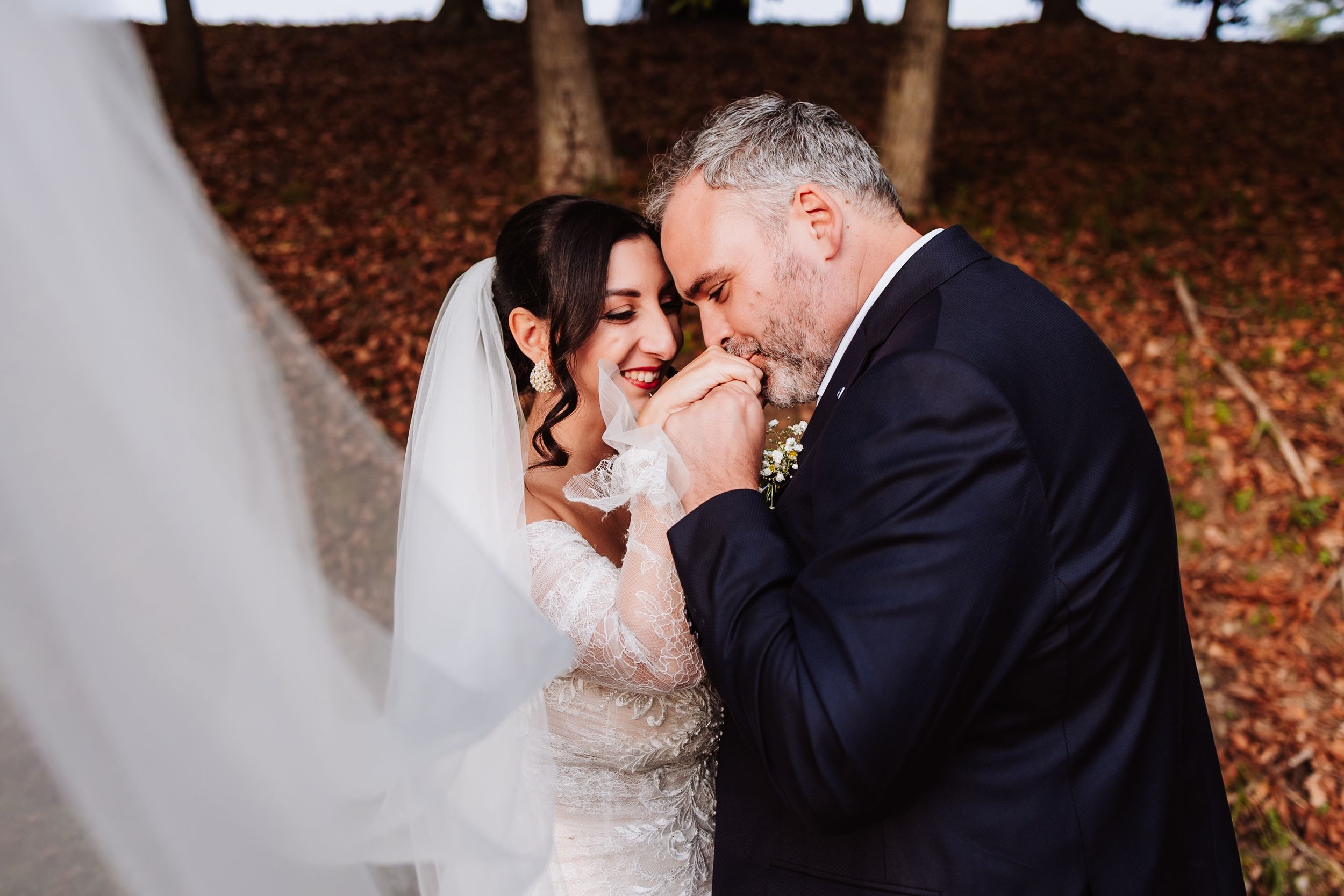 Newlywed couple shares romantic moments in autumn forest setting with fallen leaves and natural lighting.
