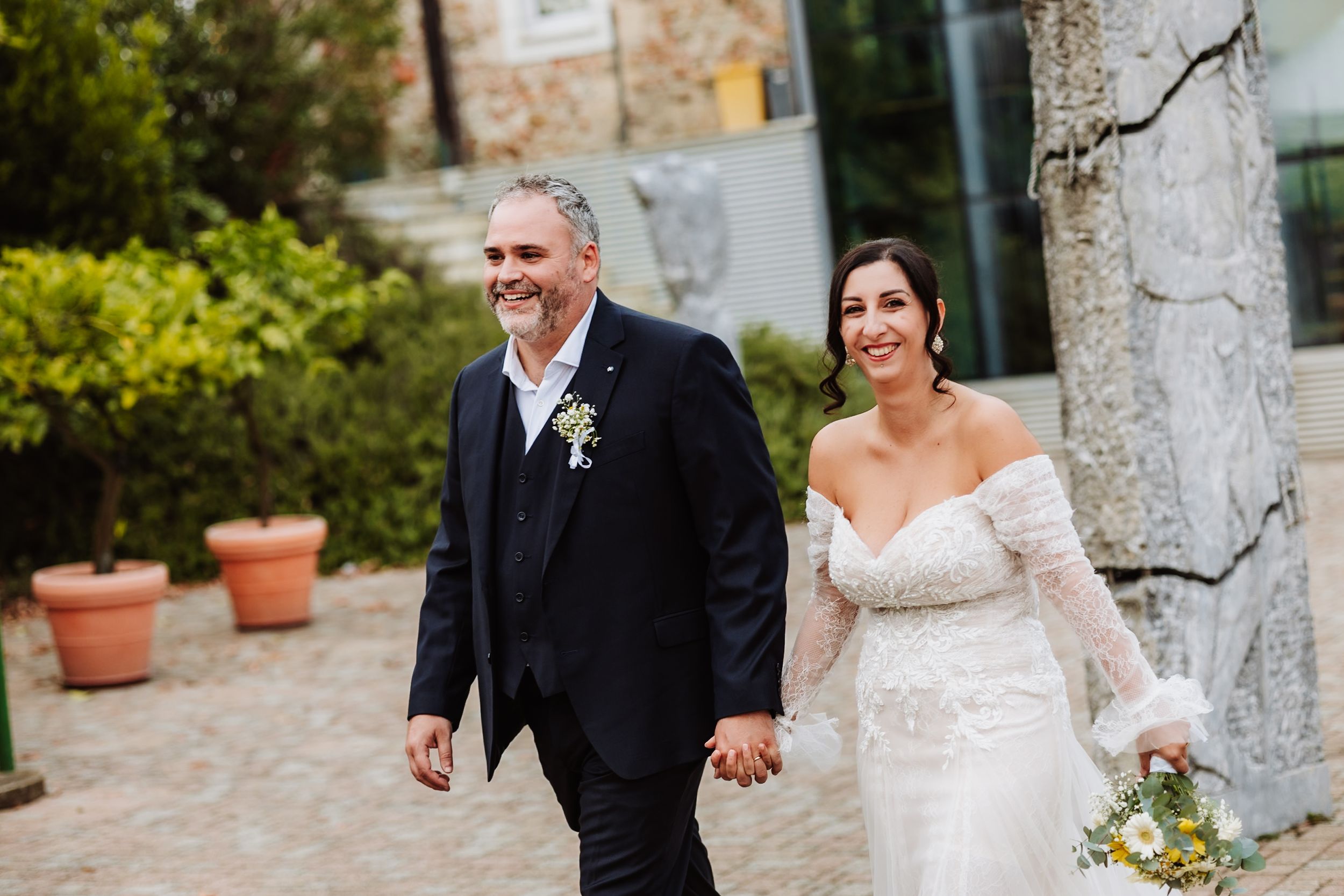 A couple in wedding attire walks hand in hand through a garden pathway on their special day.