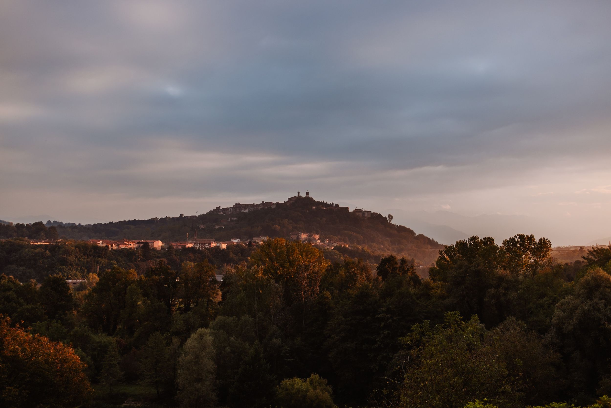 A hilltop castle silhouetted against a moody sunset sky with autumn trees in the foreground.